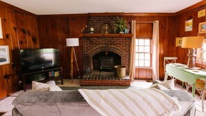 A cozy living room with a brick fireplace, a television, and a green table.