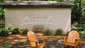 A rustic outdoor seating area with two wooden Adirondack chairs and a small wooden structure with a roof.