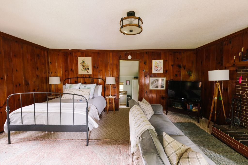 Ein gemütliches Schlafzimmer mit einem Metallbett, einem grauen Sofa, einem Fernseher und Holzwänden.