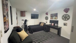 A bedroom with a bed, a desk, a sofa, a TV, and various wall decorations.