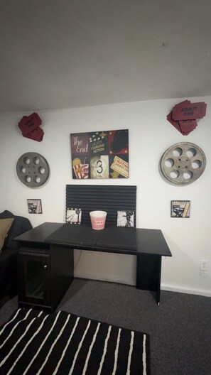 A room with a black desk, a striped rug, and a wall decorated with movie memorabilia including film reels and a poster.
