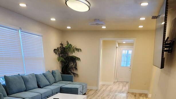 A spacious living room with a sectional sofa, a coffee table, and a large potted plant. The room has wooden flooring and recessed ceiling lighting. - 4-bedroom heated Pool house in lovely Osprey, 5 minutes to the beach (Osprey)