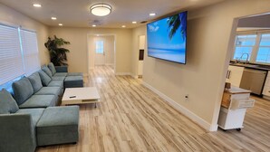 A modern living room with a sectional sofa, a flat-screen TV, and a kitchen area with a countertop and cabinets. - 4-bedroom heated Pool house in lovely Osprey, 5 minutes to the beach (Osprey)