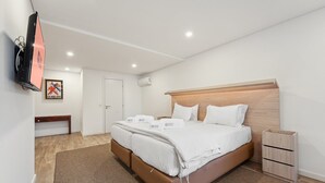 Una habitación de hotel moderna con una cama grande, cabecera de madera, un banco, un televisor y un cartel enmarcado.