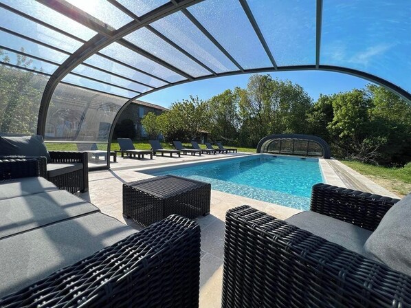 Une piscine extérieure couverte, dotée de chaises longues et d’une structure en forme de pergola.