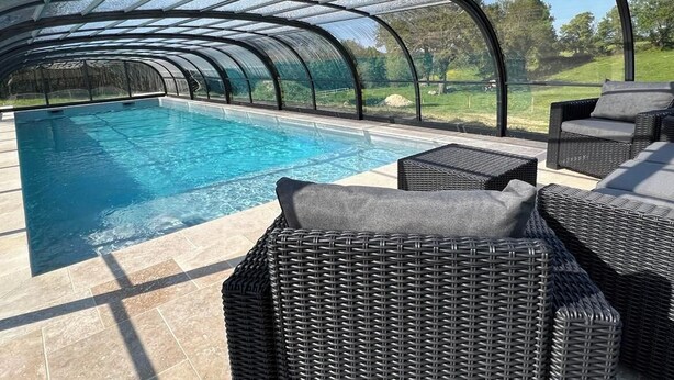 A covered swimming pool with clear glass walls, wicker furniture, and a view of the surrounding landscape. - La Millière - "Marie-Anne & Marie-Adélaïde & Charette" - Chambres indépendantes - Piscine & campagne - (Le Poiré-sur-Vie)