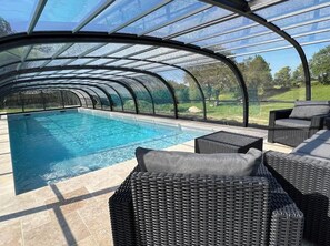 A covered swimming pool with clear glass walls, wicker furniture, and a view of the surrounding landscape. - La Millière - "Marie-Anne & Marie-Adélaïde & Charette" - Chambres indépendantes - Piscine & campagne - (Le Poiré-sur-Vie)