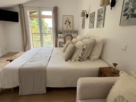 Un dormitorio con una cama grande, una mesita de noche, una silla, un escritorio y una ventana con cortinas.