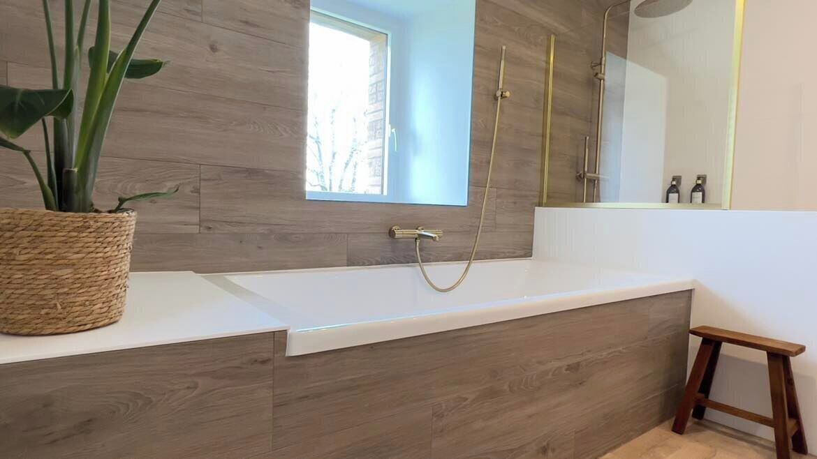 Un baño moderno con un tocador de madera, un espejo grande, una planta en maceta y un taburete pequeño de madera.