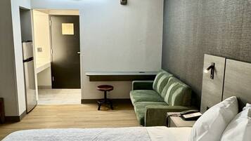 Quarto de hotel com uma cama grande, um sofá verde, uma mesa redonda pequena e uma escrivaninha com telefone.