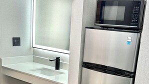 Eine moderne Küche mit einem Edelstahl-Kühlschrank, einer Mikrowelle und einer weißen Arbeitsplatte mit Waschbecken.