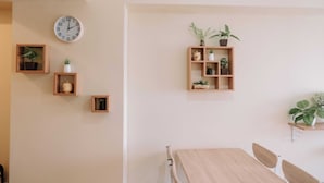 A minimalist room with a wooden dining table, a wall clock, and several shelves with plants and decorative items. - Golden Sunset Skyline Retreat (Iloilo)