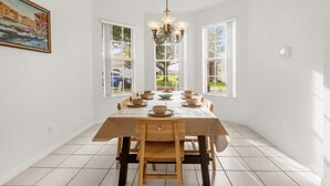 A dining room with a large wooden table, chairs, and a chandelier. There are windows on the walls, and a painting is visible on the left wall. - EV_416 - 4 Bed 3 Bath with Screened-In Private Pool, Games Room (Davenport)