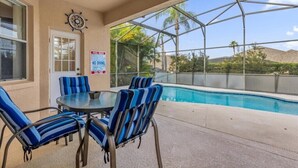 A covered outdoor area with a pool, blue-striped chairs, and a table. - EV_416 - 4 Bed 3 Bath with Screened-In Private Pool, Games Room (Davenport)