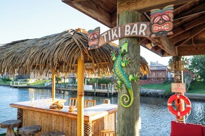 Eine Tiki-Bar mit einem Reetdach, einer Holztheke und einem Schild mit der Aufschrift 'TIKI BAR'.