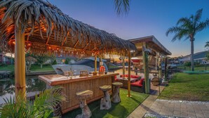 Un espace bar doté d’un toit de chaume, de tabourets en bois et situé au bord de la piscine.