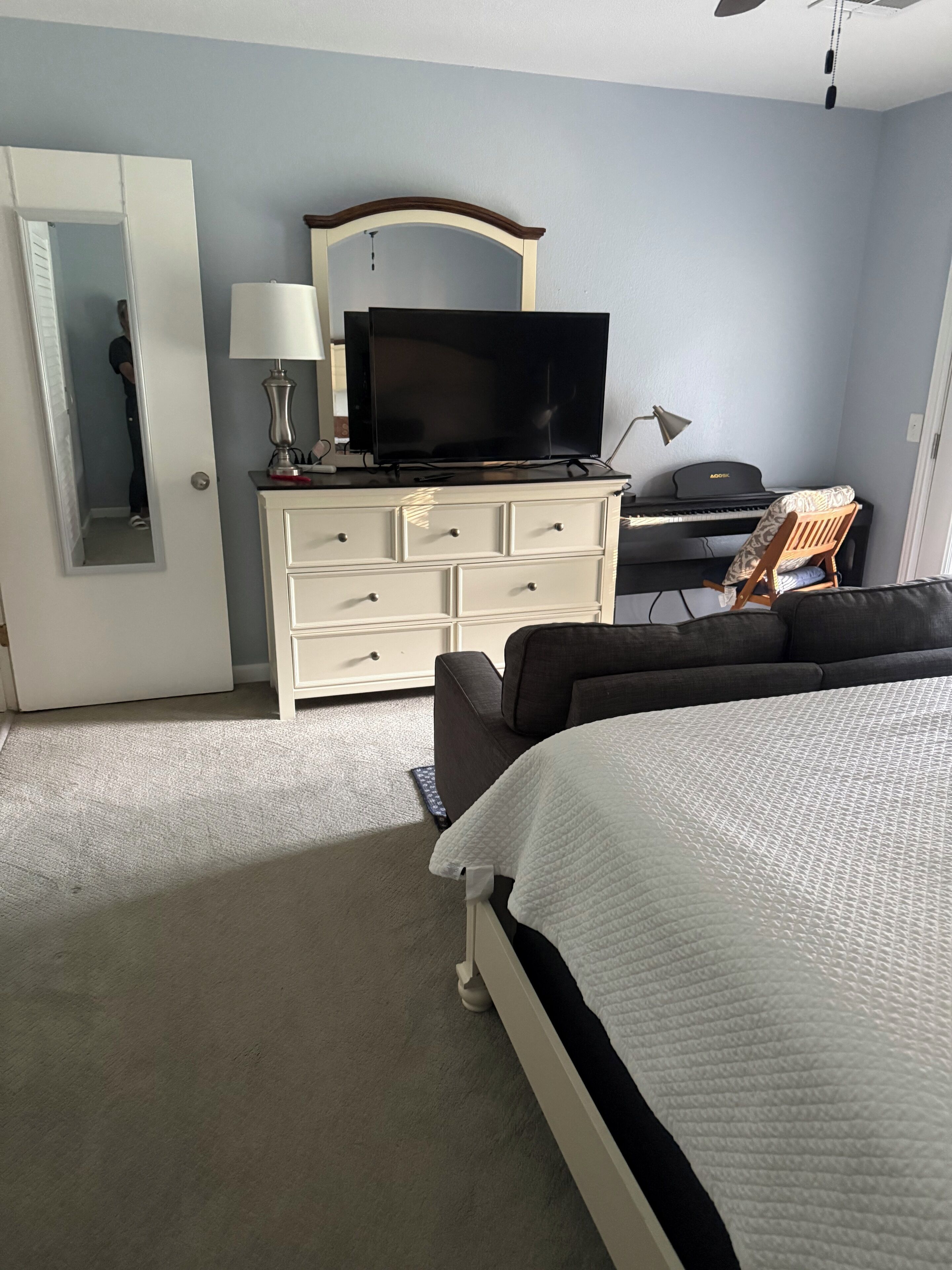 Een slaapkamer met een bed, een dressoir, een televisie, een piano en een spiegel.