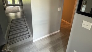 Un pasillo con suelo de madera, una puerta que da a una habitación y una pequeña alfombra.