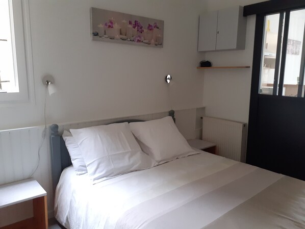 Ein Schlafzimmer mit einem Bett, Nachttischen, einem an der Wand befestigten Regal und einem Fenster.