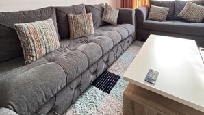 A modern living room with a grey sectional sofa, a white coffee table, and a patterned rug. - Cozy 1-bedroom apartment with WiFi, AC in awesome Swemeh (Swemeh)