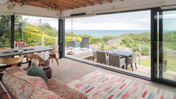 Een ruime woonkamer met een grote schuifpui die leidt naar een terras met uitzicht op zee.