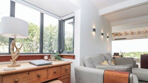 Een moderne kamer met een houten bureau, een comfortabele fauteuil, een bank en uitzicht op groen via grote ramen.