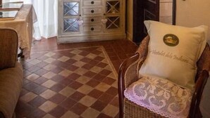 A room with a checkered floor, a wooden cabinet with drawers, a wicker chair with a cushion, and a mirror on the wall. - Hostalet dels Indians (Begur)