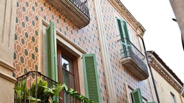 A building with a patterned facade, green shutters, and a wrought iron balcony. - Hostalet dels Indians (Begur)
