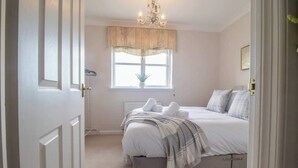 A bedroom with a bed, a window with a valance, a chandelier, and a door. - The Well - 3 bedroom apartment (Motherwell)