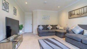 A living room with a sectional sofa, a flat-screen TV, a glass coffee table, and a painting on the wall. - The Well - 3 bedroom apartment (Motherwell)