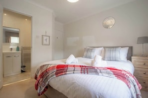 A bedroom with a bed, a bedside table, a lamp, a wall clock, and a framed picture. - The Well - 3 bedroom apartment (Motherwell)