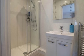 A bathroom with a glass-enclosed shower, a white sink with a blue bottle, and a mirror above the sink.