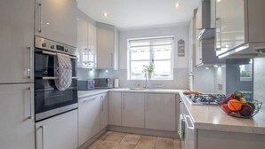 A modern kitchen with stainless steel appliances, a large window, and a fruit bowl on the counter. - The Well - 3 bedroom apartment (Motherwell)