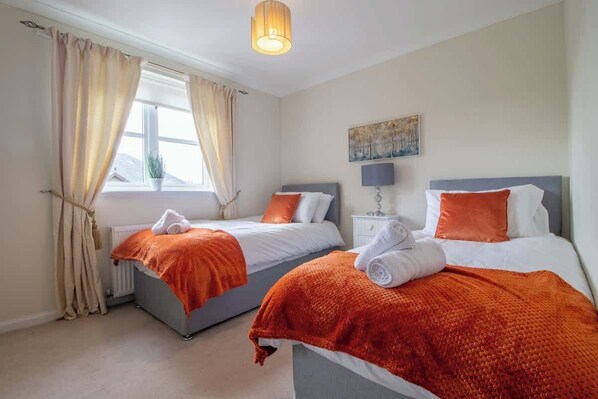 Habitación de hotel con dos camas, una ventana con cortinas, un cuadro en la pared y una lámpara en una mesita de noche.