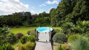 A wooden deck leading to a circular pool surrounded by lush greenery and trees. - Storm Cabin by Contemporary Hotels (Bangalow)