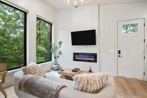 A modern living room with a large window, a flat-screen TV, a fireplace, and a cozy sofa. - Cliffside View | Modern Couples Retreat, Hot Tub (Rockbridge)