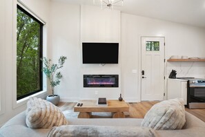A modern living room with a fireplace, a flat-screen TV, a dining table, and a sofa. - Cliffside View | Modern Couples Retreat, Hot Tub (Rockbridge)