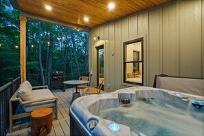 A hot tub on a wooden deck with a view of trees, a table and chairs, and a door leading to an interior room. - Cliffside View | Modern Couples Retreat, Hot Tub (Rockbridge)