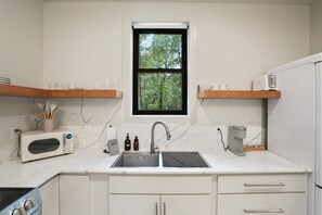 A modern kitchen with a double sink, a microwave, a coffee maker, and a window with a view of trees. - Cliffside View | Modern Couples Retreat, Hot Tub (Rockbridge)