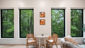 Un salón moderno con ventanas amplias, una mesa redonda, dos sillas de madera y un sofá.