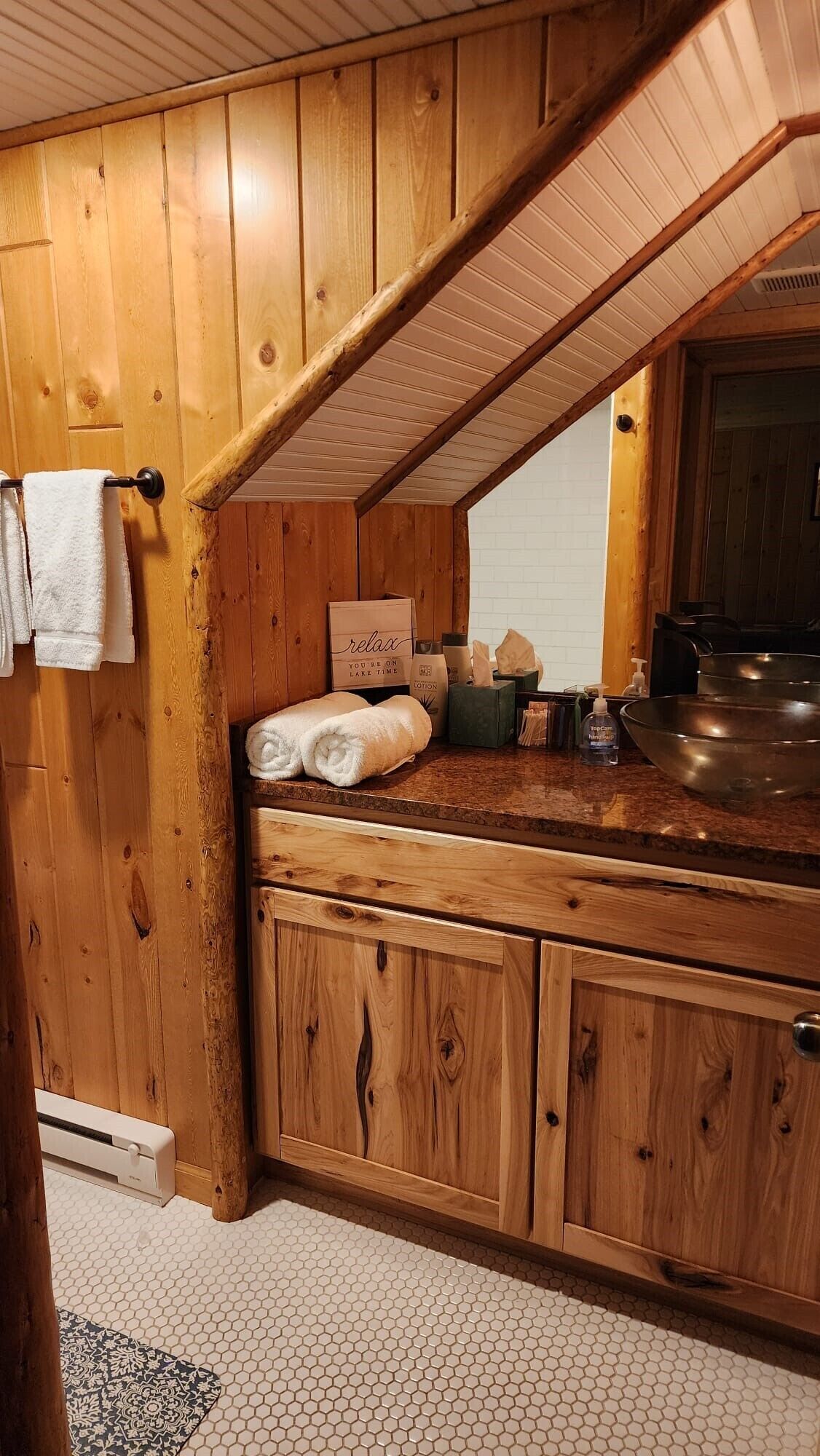A wooden cabin interior with a kitchen area, including wooden cabinets, a countertop, and a large metal bowl.