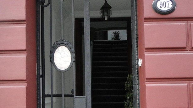 Un bâtiment rouge avec une porte noire, une plaque d’immatriculation blanche et un sol à carreaux noirs et blancs.