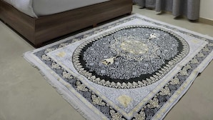 Une chambre à coucher avec un lit, des rideaux gris, un tapis à motifs et un climatiseur fixé au mur.