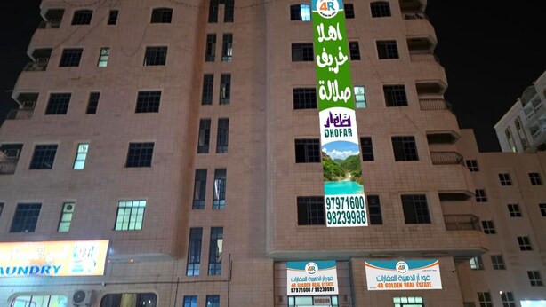 Un immeuble à plusieurs étages, orné de nombreuses enseignes, dont une grande banderole verte qui fait la publicité d’une société immobilière.