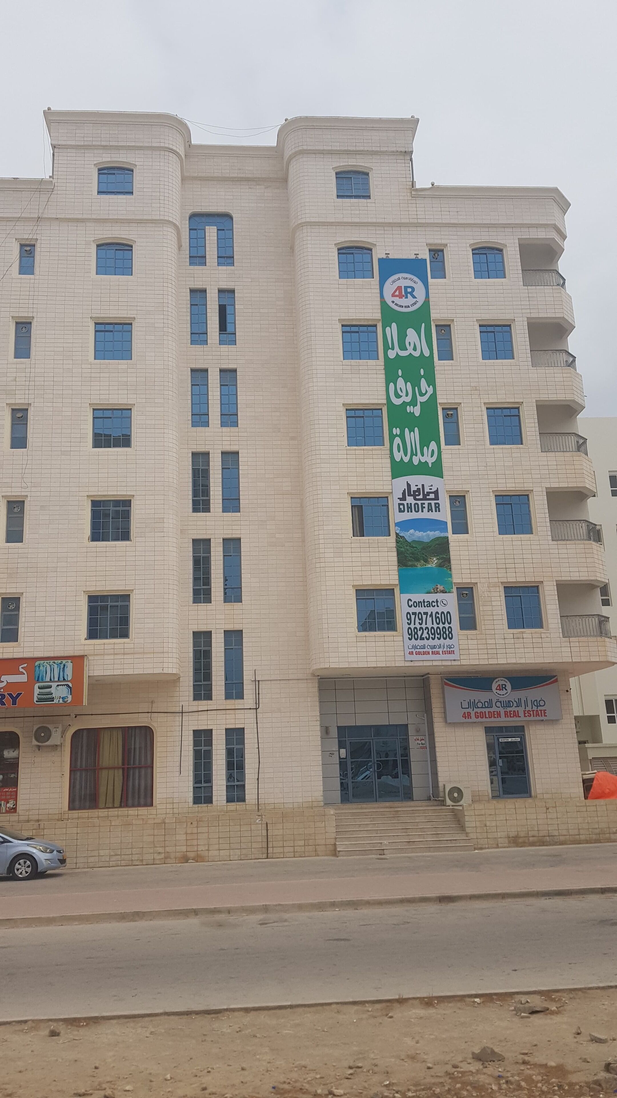 Un edificio de varios pisos con un llamativo letrero verde que anuncia una empresa inmobiliaria.