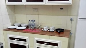 Une cuisine de taille réduite avec des meubles blancs, un plan de travail sur lequel se trouvent de la vaisselle et des bouteilles d’eau, et une cuisinière.