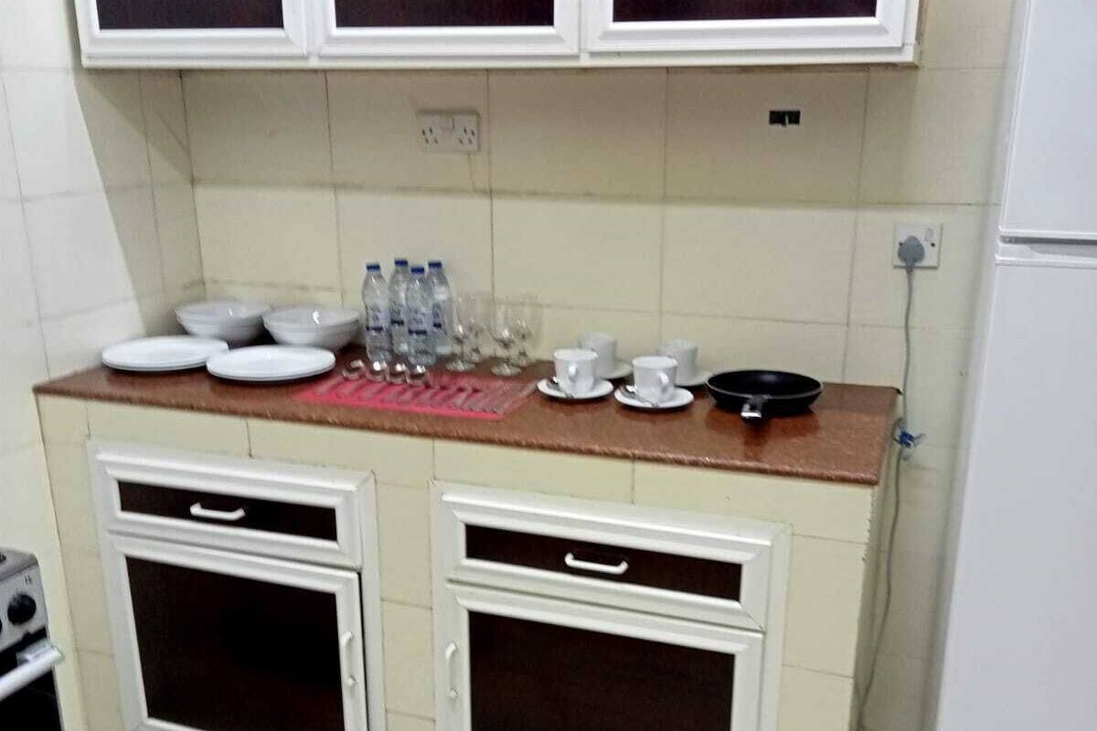A compact kitchen with white cabinets, a countertop with dishes and water bottles, and a stove.