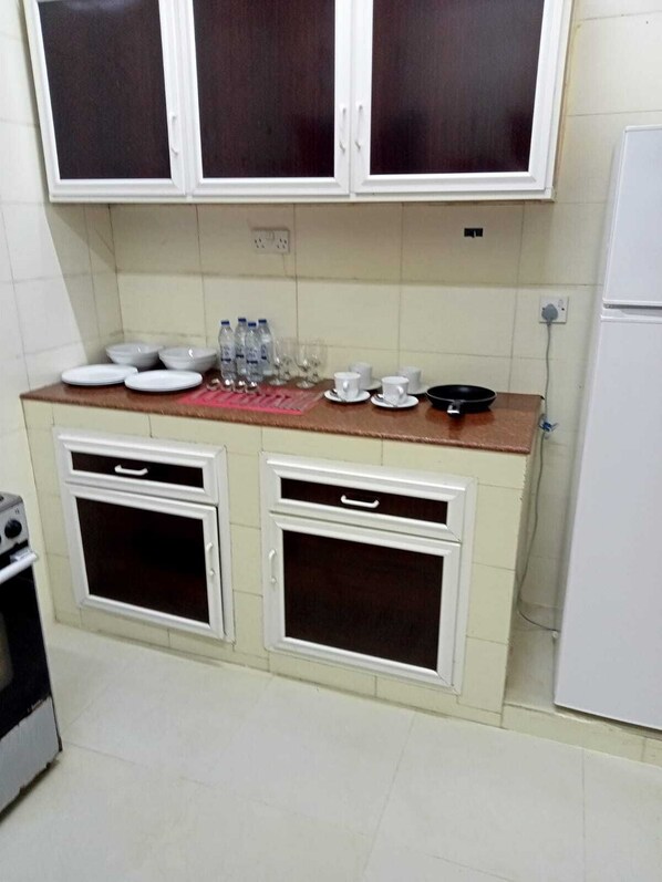 A compact kitchen with white cabinets, a countertop with dishes and water bottles, and a stove.