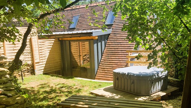 Une cabane en bois avec une porte en verre, un jacuzzi et un chemin en pierre.