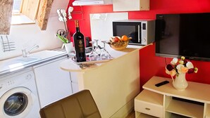 Une cuisine compacte équipée d’un lave-linge, d’un four à micro-ondes, d’une télévision et d’un petit coin repas agrémenté d’un vase de fleurs.